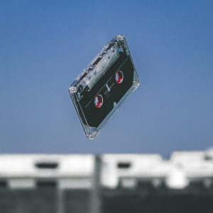 A Retro Cassette Tape Floats In Mid Air With A Blurred Urban Background, Symbolizing Nostalgia.