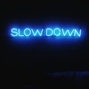 A Glowing Blue Neon Sign Reads 'Slow Down' Against A Dark Backdrop, Creating A Modern Aesthetic.