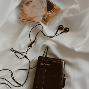 A Classic Sony Walkman With Cassette Tapes And Earphones On A White Bed, Showcasing Retro Vibes.