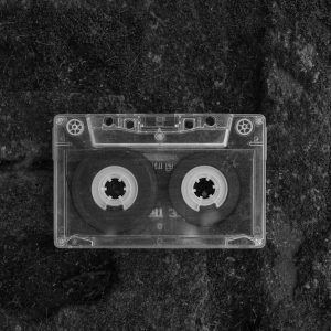 A Nostalgic Black And White Close Up Of A Cassette Tape On A Textured Surface, Evoking Retro Vibes.