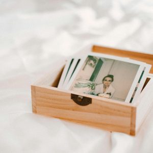 A Wooden Box Holding Vintage Polaroid Photos On A Soft White Surface, Evoking Nostalgia.