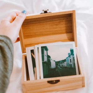 A Hand Opening A Wooden Box Containing Vintage Polaroid Photos On A White Sheet.