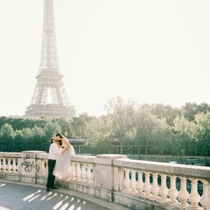 A Couple Embraces On A Bridge With The Iconic Eiffel Tower In The Background, Embodying Romance In Paris.