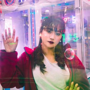 Young Woman In A Red Jacket At An Arcade Game Surrounded By Neon Lights.