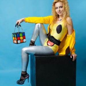 Stylish Woman In 80s Fashion Attire Posing With A Colorful Cube Bag.