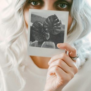 Close Up Of A Young Woman With Blonde Hair Holding A Polaroid Photo.