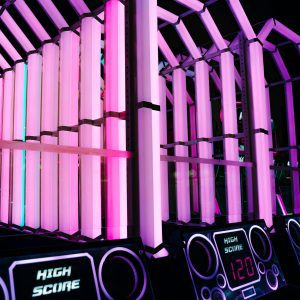 A Brightly Lit Arcade Game With Neon Pink Lights And High Scores Displayed On Screens.