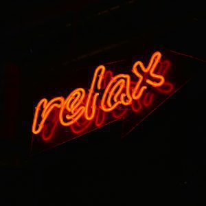A Glowing Red Neon 'relax' Sign Against A Black Background, Perfect For Modern Decor.