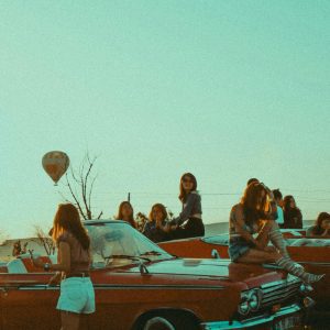 Group Of Women Enjoying A Sunset With Classic Cars And A Hot Air Balloon In Cappadocia, Türkiye.