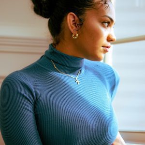 Portrait Of A Woman In A Blue Turtleneck Gazing Out A Window, Exuding Elegance.
