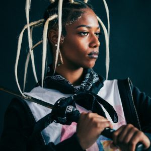 Portrait Of A Fashionable Woman With A Distinctive Hairstyle, Holding A Sword, Captured In A Studio Setting.