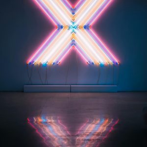 Vibrant Neon X Sign With Colorful Reflections On A Dark Floor Background.