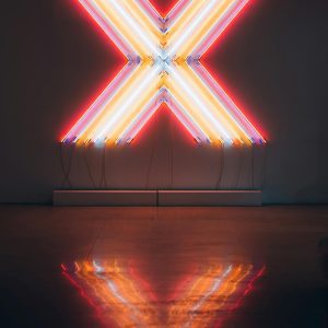 Vibrant Neon X Sign Illuminating A Dark Room, Reflecting On The Floor.