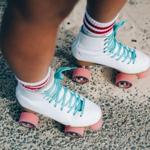 White Roller Skates With Blue Laces And Pink Wheels On A Textured Outdoor Surface.