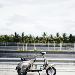 Classic Rusty Scooter Parked On A Tropical Road With Palm Trees Under A Cloudy Sky.