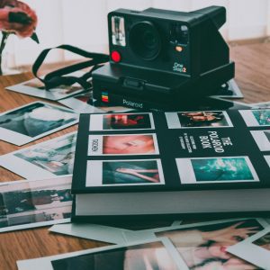 A Vintage Polaroid Camera With Scattered Instant Prints And A Photo Album On A Wooden Table.