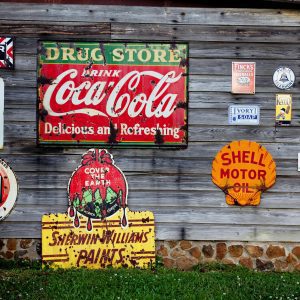 Collection Of Vintage Advertising Signs On Rustic Wooden Wall Showcasing Classic Brands.