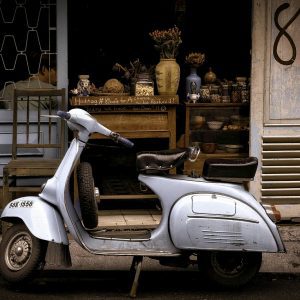 A Classic Vespa Scooter Parked In Front Of A Charming Café, Evoking Retro Vibes.