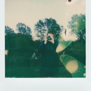 A Nostalgic Polaroid Photo Capturing A Person With A Camera In A Natural Outdoor Setting.