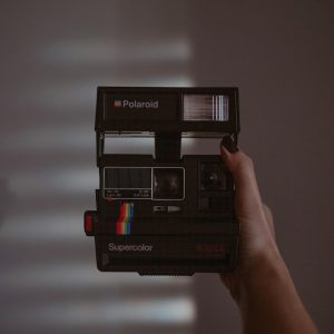 Hand Holding A Vintage Polaroid Camera Indoors With Dramatic Shadow Lighting.