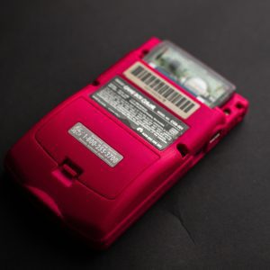 A Vibrant Red Retro Portable Game Console Photographed On A Dark Surface.