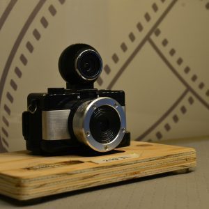 Close Up Of A Vintage Analog Camera On A Wooden Base Against A Retro Backdrop.