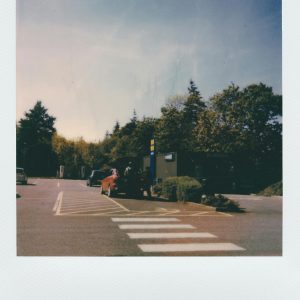 Vintage Polaroid Photo Featuring A Quiet Parking Lot Scene With Cars, Trees, And A Hazy Sky.