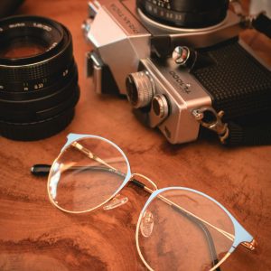 A Vintage Camera And Eyeglasses Resting On A Wooden Surface With A Warm Atmosphere.