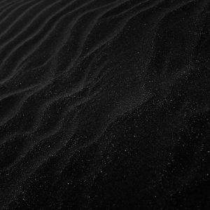 Textured Black Sand With Ripples Resembling Dunes, Creating A Dark, Abstract Aesthetic.