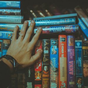 A Hand Reaching For A Classic VHS Tape From A Colorful Vintage Collection Indoors.