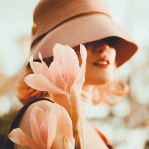 Portrait Of A Woman Wearing A Stylish Hat, Holding Pink Lilies Under Soft Lighting.