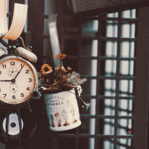A Rustic Alarm Clock Hanging Beside Flowers In A Vintage Setting.