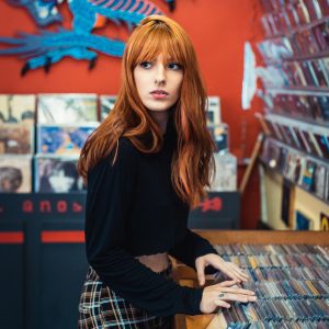 A Woman With Red Hair Explores A Vibrant Music Store Showcasing Various Albums.