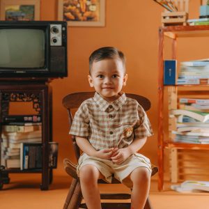 Adorable Toddler Sitting On A Wooden Chair In A Retro Styled Orange Room.