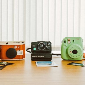 A Collection Of Vintage And Instant Cameras On A Wooden Table With Printed Photos.