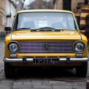Front View Of A Vintage Yellow Car Parked On A Cobblestone Street In Lviv, Ukraine.