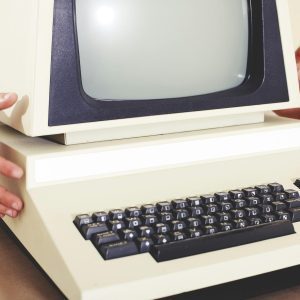 A Vintage Computer With A Classic CRT Monitor And Keyboard, Being Held By Hands.