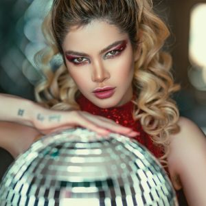 Stylish Woman With Expressive Eyes Poses With A Disco Ball, Glamorous Makeup Enhancing Her Features.