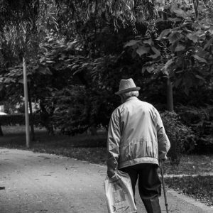 Elderly Man In A Hat Walking On A Park Path With A Cane, Captured In Monochrome.