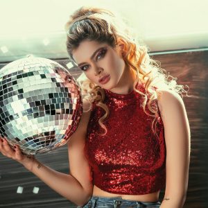 Stylish Woman In Red Sequin Top Holding A Disco Ball, Exuding Glamour And Allure.
