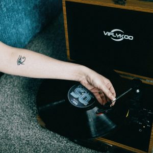 A Hand With A Tattoo Lowers The Needle Onto A Vinyl Record In A Vintage Turntable Setting.