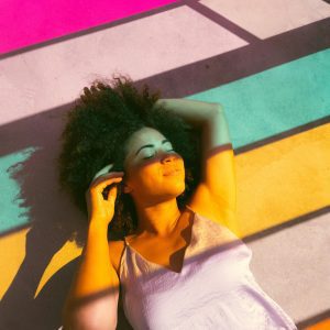 Woman Relaxing On A Colorful Sunlit Floor With Shadows Creating Vibrant Patterns.
