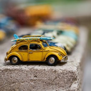 Close Up Of A Yellow Vintage Toy Car With A Surfboard On A Concrete Surface.