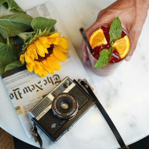Artful Flat Lay Of A Vintage Camera, Sunflower, And Refreshing Drink On A Table.