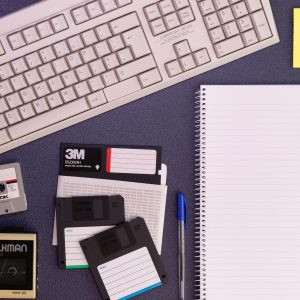 Vintage Office Setup Featuring A Compaq Keyboard, Floppy Disks, Cassette Tape, And Notepad.