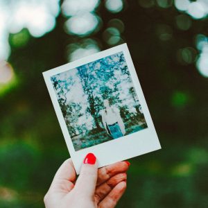 Close Up Of A Hand Holding An Instant Polaroid Photo With A Blurred Outdoor Background.
