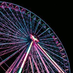 A Brightly Illuminated Ferris Wheel With Vibrant Lights Stands Tall Against The Night Sky In A Theme Park.
