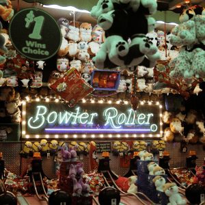 Exciting Indoor Carnival Game Setting Featuring Vibrant Plush Toys And A Glowing 'Bowler Roller' Sign.