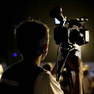 A Cameraman Filming An Event Outdoors At Night With Professional Equipment, Capturing The Vibrant Atmosphere.
