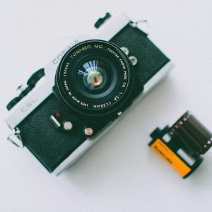 Close Up Of A Classic Film Camera And Roll On A White Background, Showcasing Vintage Photography Equipment.